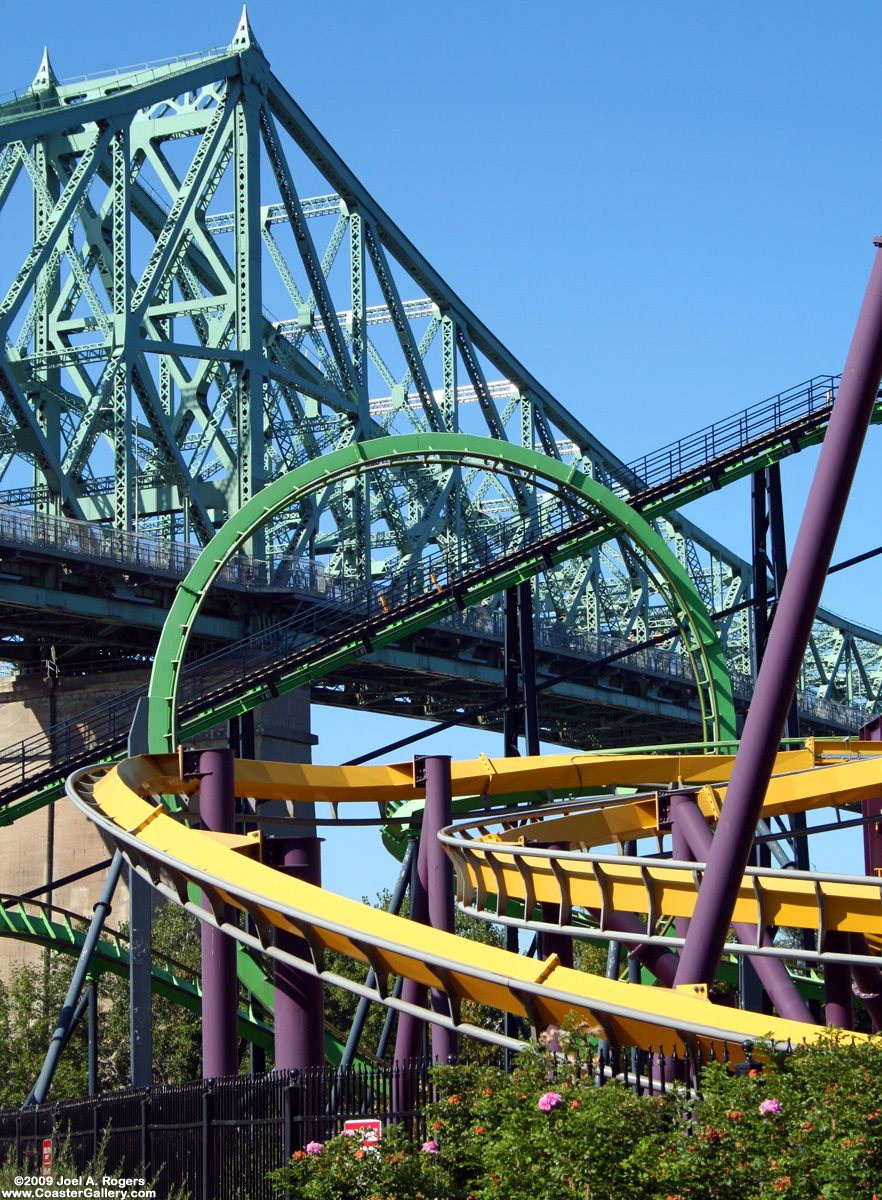 Two roller coasters in front of a bridge