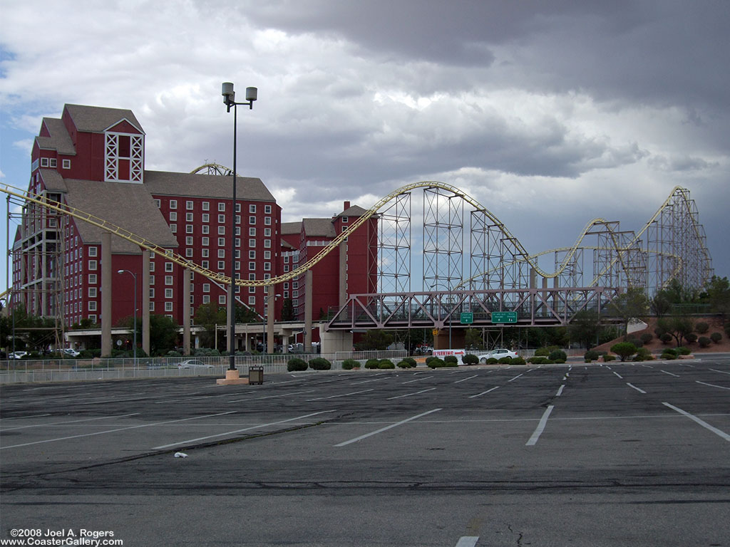 A yellow steel roller coaster going around a hotel