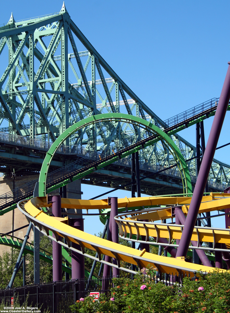 Two roller coasters in front of a bridge